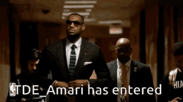 a man in a suit and tie is walking down a hallway with a caption that says tde amari has entered .