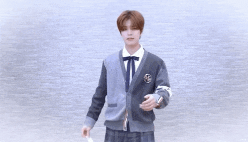a young man in a school uniform is holding something in his hand and looking at the camera .