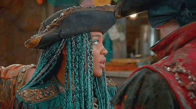 a woman with blue braids and a pirate hat looks at a man in a red jacket