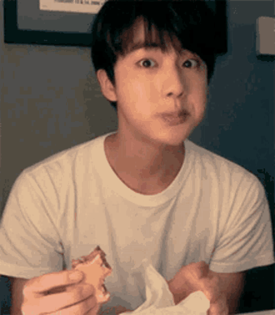 a young man in a white t-shirt is eating a cookie .