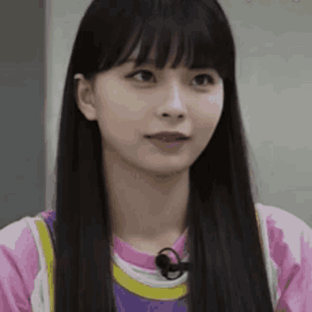 a woman with long black hair and bangs is wearing a pink and purple shirt and a microphone .