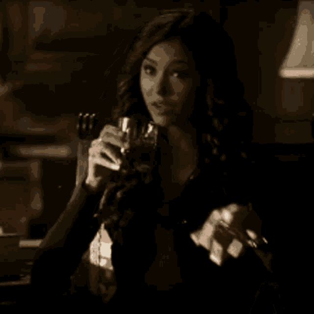 a woman is sitting in a dark room holding a glass of wine
