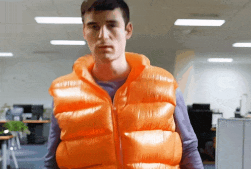 a man wearing an orange vest stands in a room