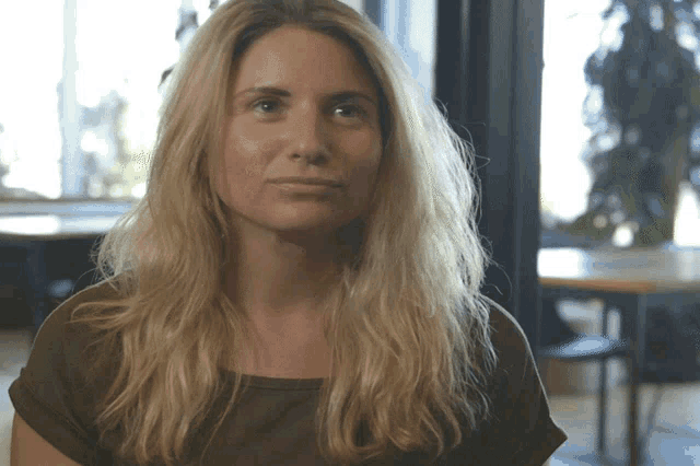 a woman with long blonde hair wearing a green shirt looks at the camera