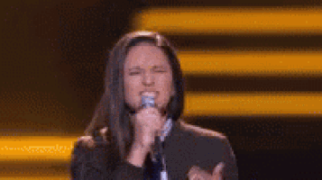 a woman is singing into a microphone on a stage while wearing a hood .
