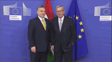 two men standing in front of flags with the european commission in the background