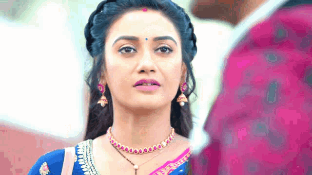 a woman wearing a necklace and earrings looks at a man .