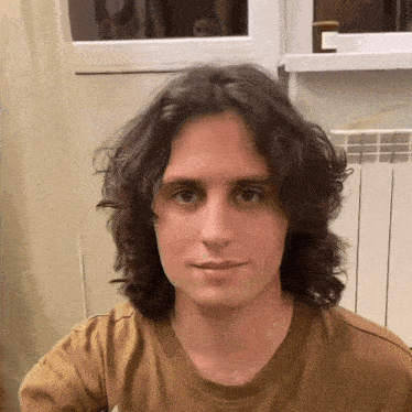a young man with long curly hair is wearing a brown t-shirt .
