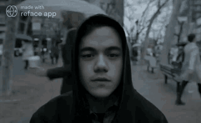 a man in a hoodie is standing on a sidewalk in front of a crowd of people .