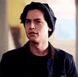 a young man wearing a knitted hat and a black shirt is looking at the camera .