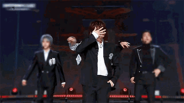 a man in a suit and white shirt is dancing on a stage with other men .
