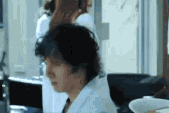 a man in a lab coat is sitting in front of a computer while a woman brushes his hair .