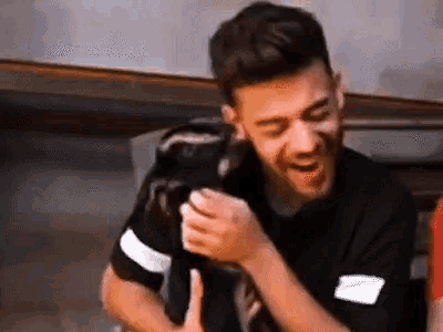 a man in a black shirt is laughing while holding a monkey in his hands .