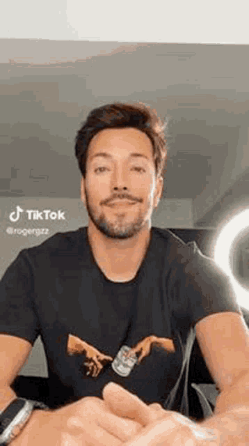 a man with a beard is wearing a black t-shirt with a picture of the creation of adam .
