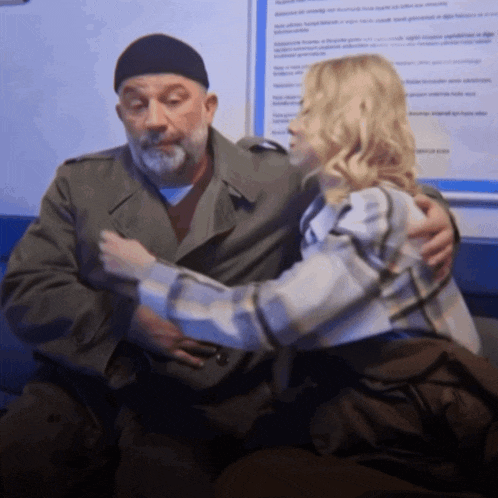 a man and a woman are hugging in front of a blue sign