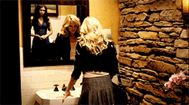 a woman standing in front of a sink looking at herself in the mirror