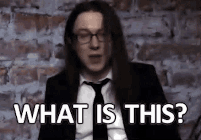 a man in a suit and tie with long hair is asking what is this .