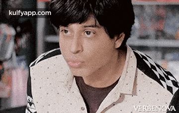 a young man is making a funny face in a store while wearing a checkered shirt .