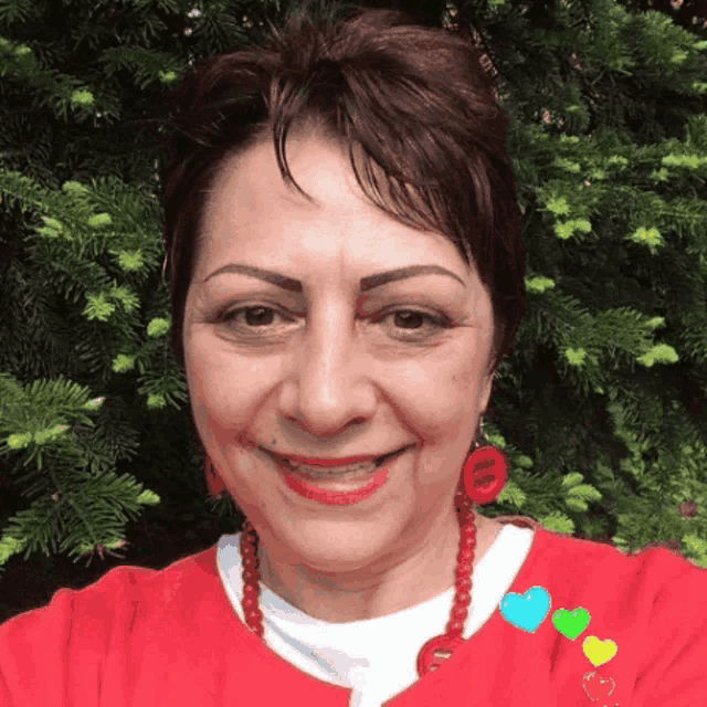a woman wearing red earrings that say i love you smiles in front of a christmas tree