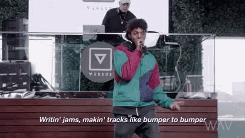 a man in a colorful jacket is singing into a microphone while a dj plays music behind him .