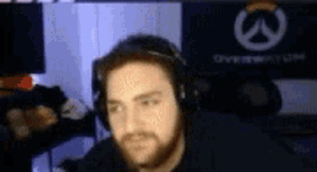 a man with a beard wearing headphones is sitting in front of a computer screen .