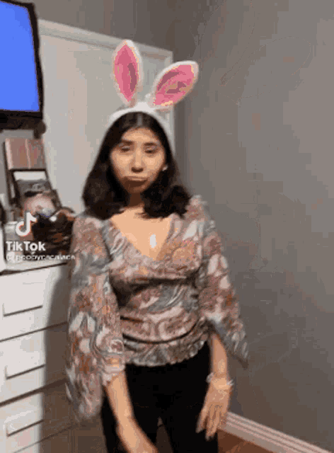 a woman wearing bunny ears is standing in front of a television in a room .