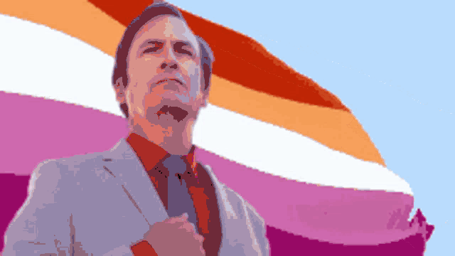 a man in a suit and tie is standing in front of a pink and orange flag
