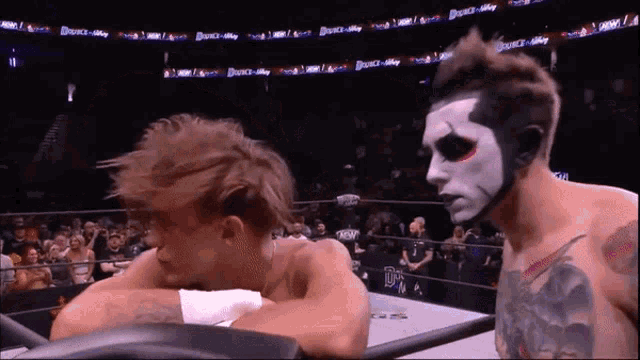 a wrestler with a face painted like a skeleton is looking at another wrestler