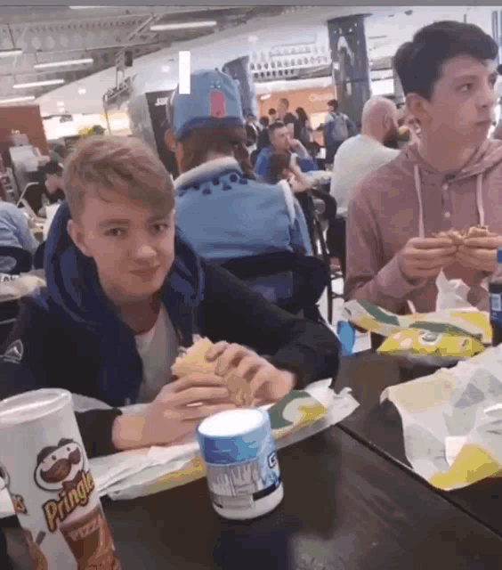 a can of pringles sits on a table in front of a boy eating a sandwich