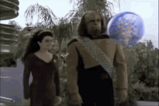 a man and a woman are standing next to each other in front of a balloon with a face on it .
