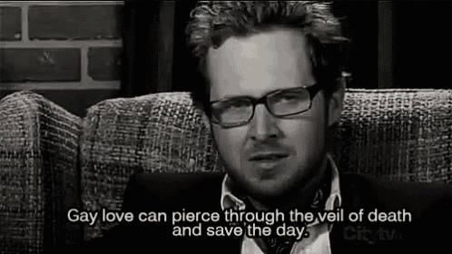a man wearing glasses and a tie is sitting on a couch and talking about gay love .