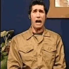 a man in a tan shirt is making a funny face while standing in front of a blue wall .