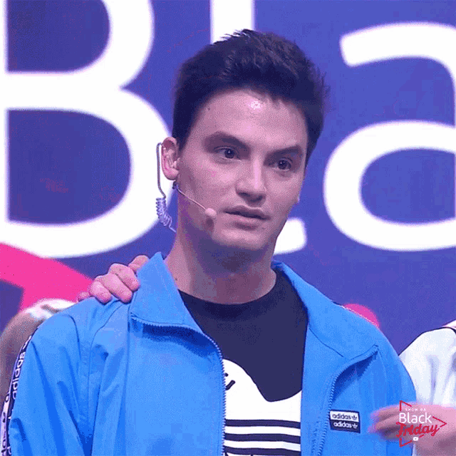 a man wearing a blue adidas jacket stands in front of a large b