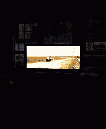 a television screen shows a tractor plowing a field