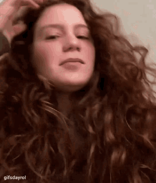 a woman with long red curly hair is holding her hair and making a funny face .
