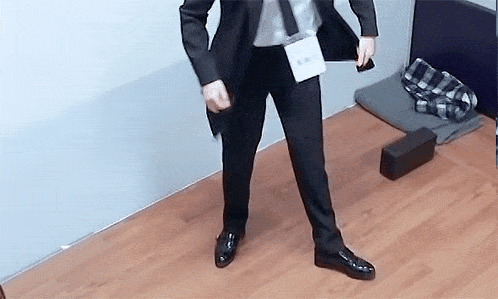 a man in a suit and tie is standing on a wooden floor and holding a cell phone .