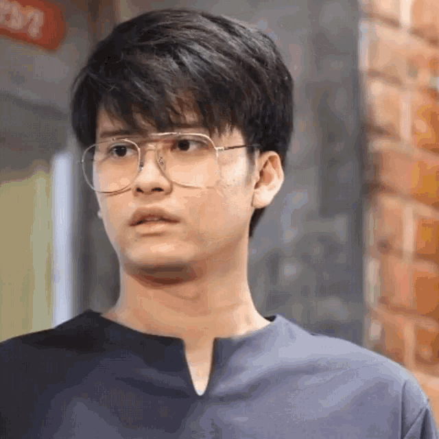a young man wearing glasses and a blue shirt is standing in front of a brick building .