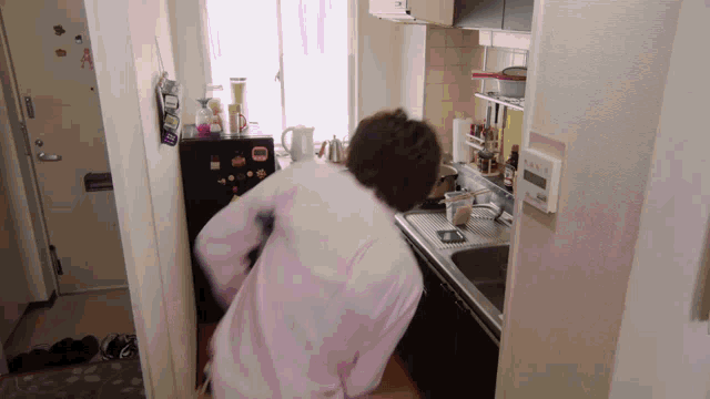 a man in a pink shirt is standing in a kitchen with a black refrigerator