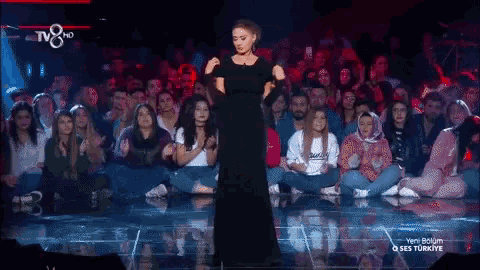 a woman in a black dress is standing on a stage in front of a crowd with tv8 hd written on the bottom