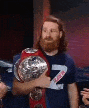 a man with a beard is holding a wrestling championship belt in his hands .