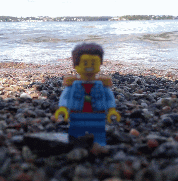 a lego figure standing on a rocky beach near the water