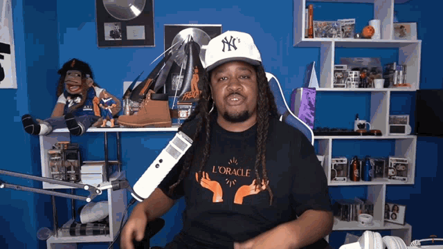 a man wearing a ny hat and a l' oracle shirt talks into a microphone
