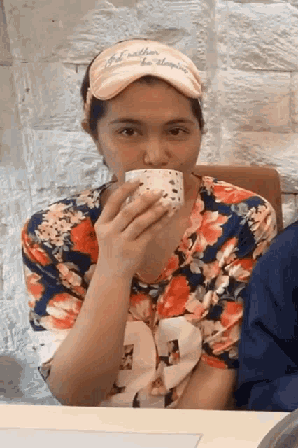 a woman wearing a hat that says " i 'd rather be sleeping " is drinking from a cup