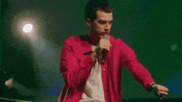a man in a red jacket is singing into a microphone on a stage