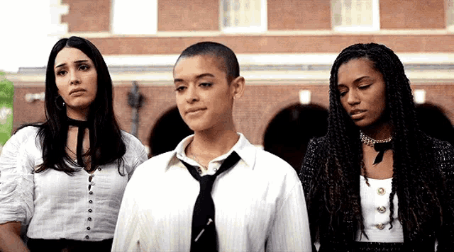 three women are standing next to each other in front of a building .