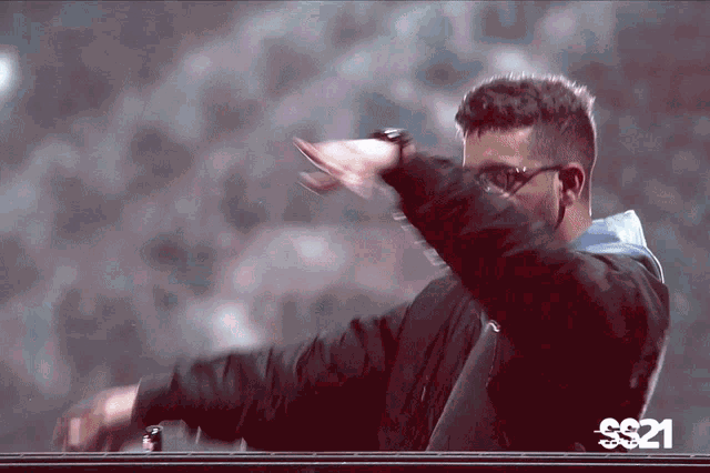 a man wearing sunglasses and a black jacket is dancing in front of a sign that says s321