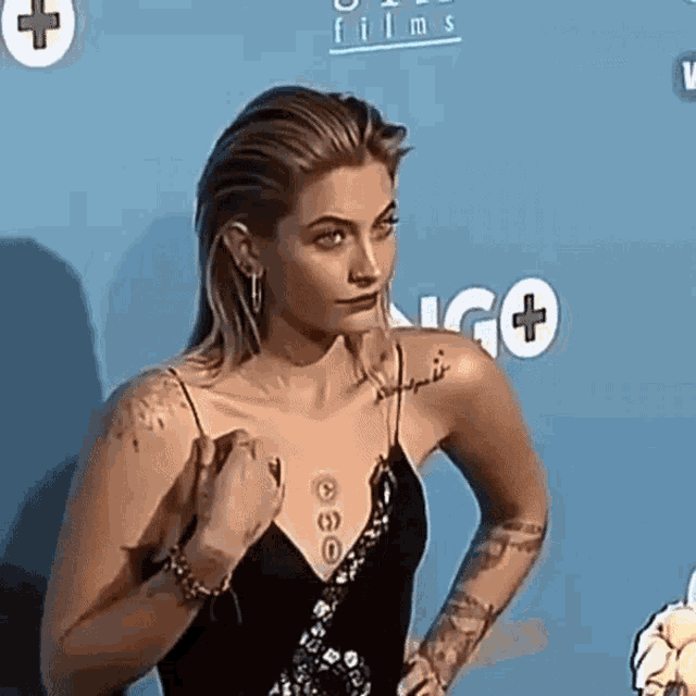 a woman with a tattoo on her shoulder stands on a blue carpet in front of a sign that says films