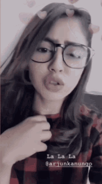 a woman wearing glasses and a plaid shirt singing la la la