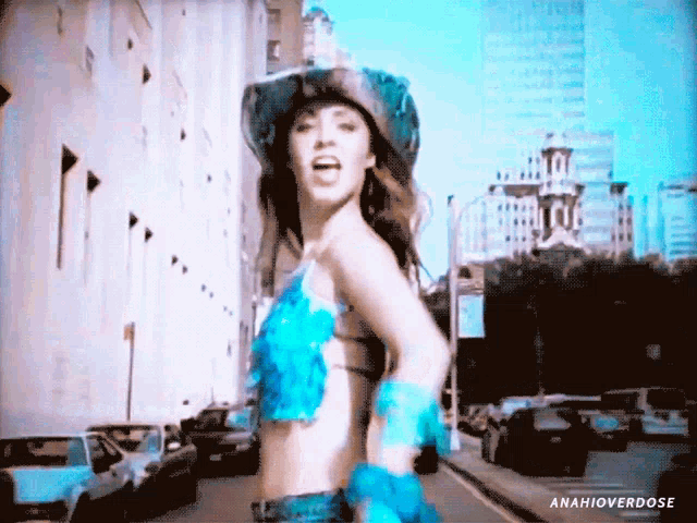 a woman wearing a cowboy hat and a blue top is dancing on a city street