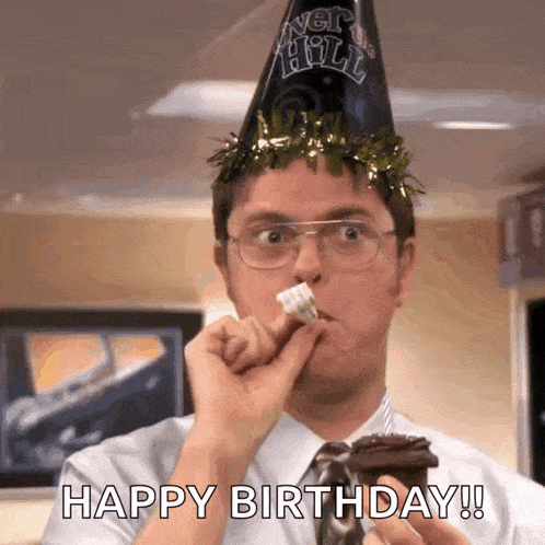 a man wearing a party hat and glasses is eating a cupcake .